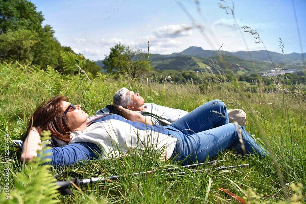 Senior couple relaxing in field on hiking day Senior couple relaxing in field on hiking day
