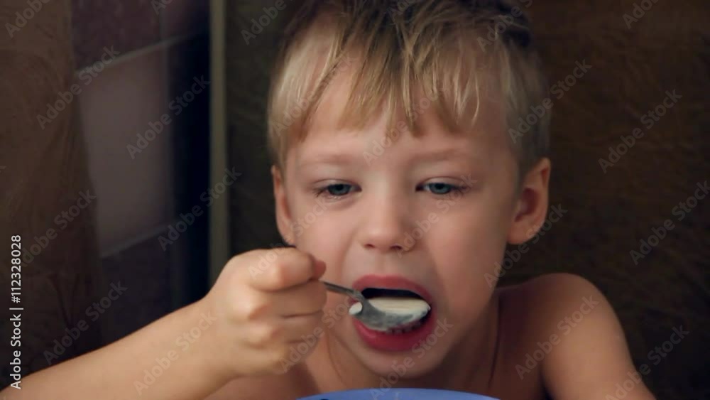 Closeup of face of little cute boy eating porridge at home kitchen. 4 years old small kid having healthy meal with appetite. Boy sitting alone at table and open wide his mouth while eating tasty food. Closeup of face of little cute boy eating porridge at home kitchen. 4 years old small kid having healthy meal with appetite. Boy sitting alone at table and open wide his mouth while eating tasty food.