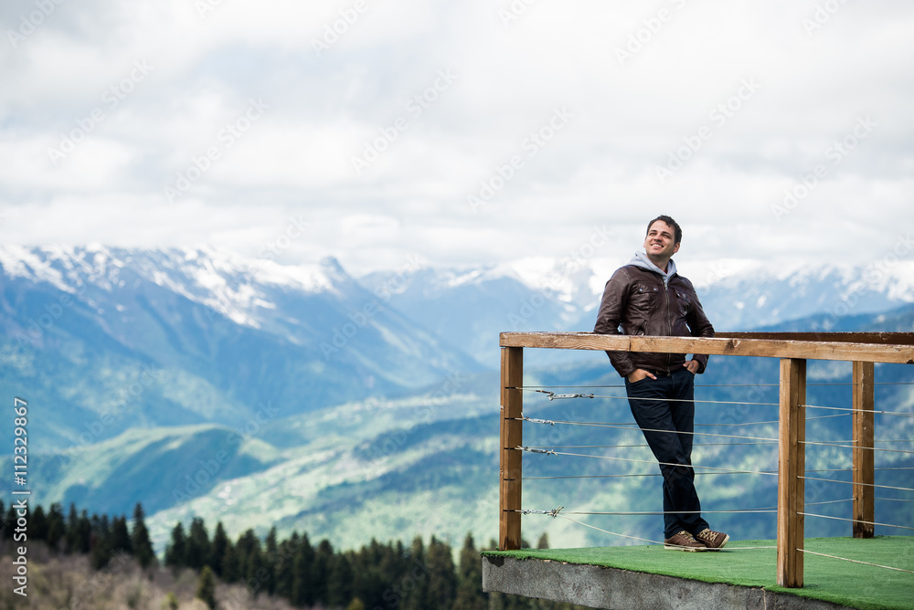 Man at view point in the mountains. Happy and smiling, looking to the sky.