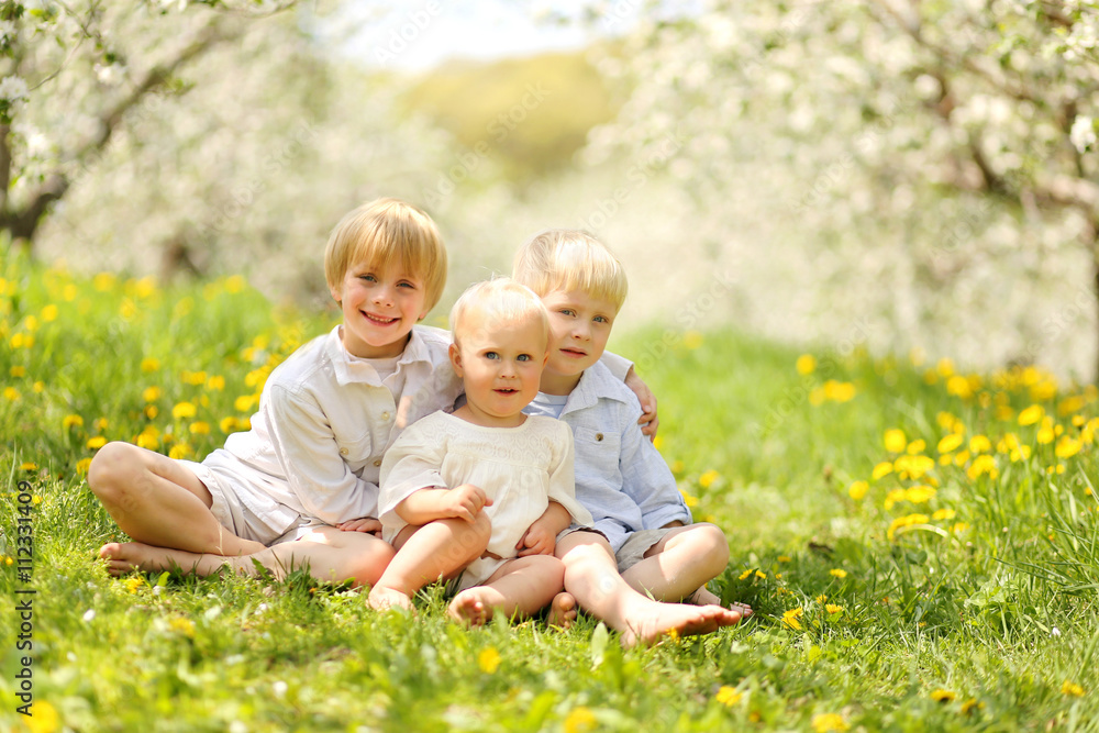 Three Cute Children Relaxing in Flower Meadow and Trees Three Cute Children Relaxing in Flower Meadow and Trees