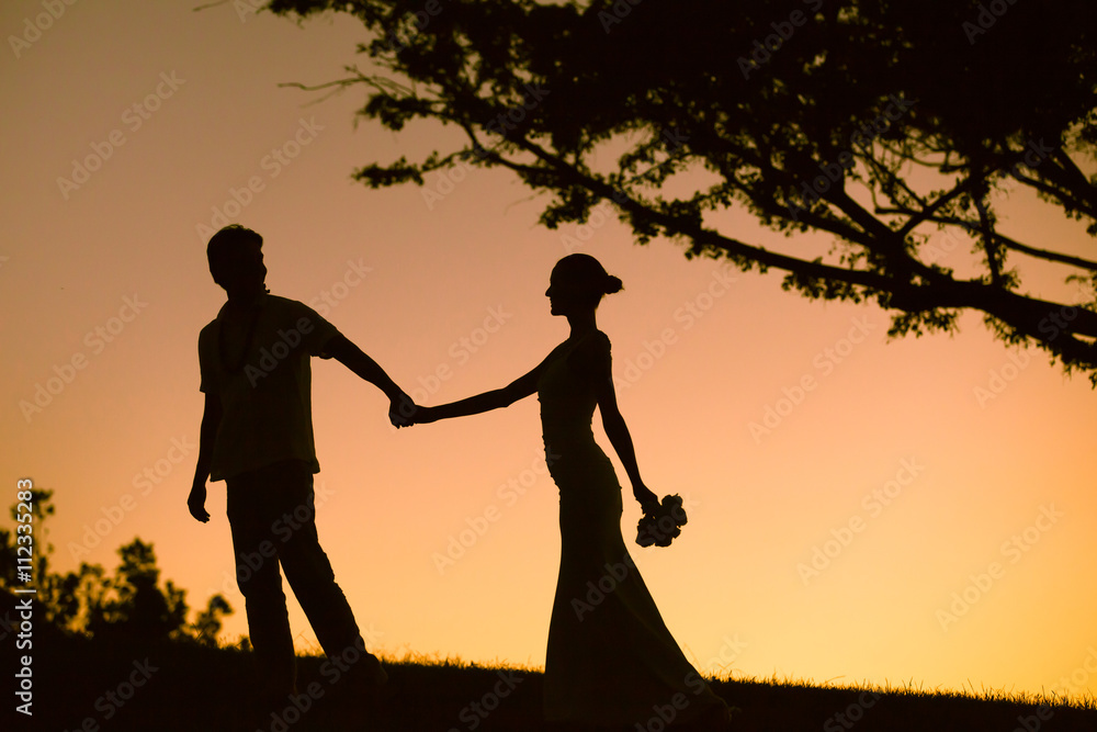 Beautiful bride and groom holding hands and walking in the sunset. 