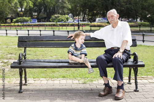 great grandfather sitting on a bench in park with his grandson