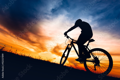 silhouette of biker boy riding mountain bike on hills at sunset