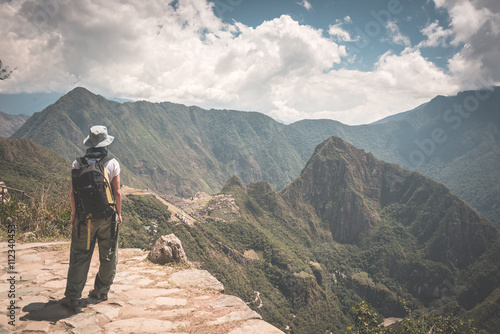 Backpacker standing in contemplation on the Inca Trail above Machu Picchu, the most visited travel destination in Peru. Rear view, toned, desaturated and vintage styled image.