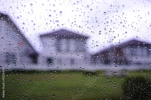Raindrops on glass of car with blurry village in overcast day