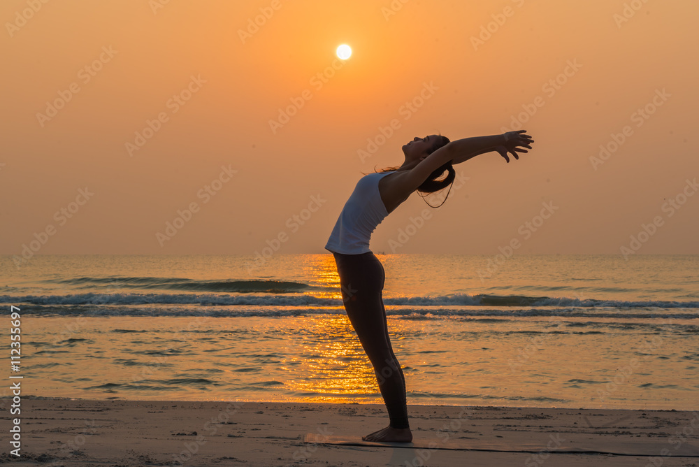 Silhouette young woman practicing yoga on the beach at sunrise. 