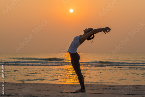 Silhouette young woman practicing yoga on the beach at sunrise. 