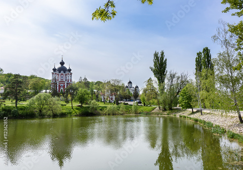 Orthodox Curchi monastery in Moldova with gren trees and blue sky, with reflection on the lake