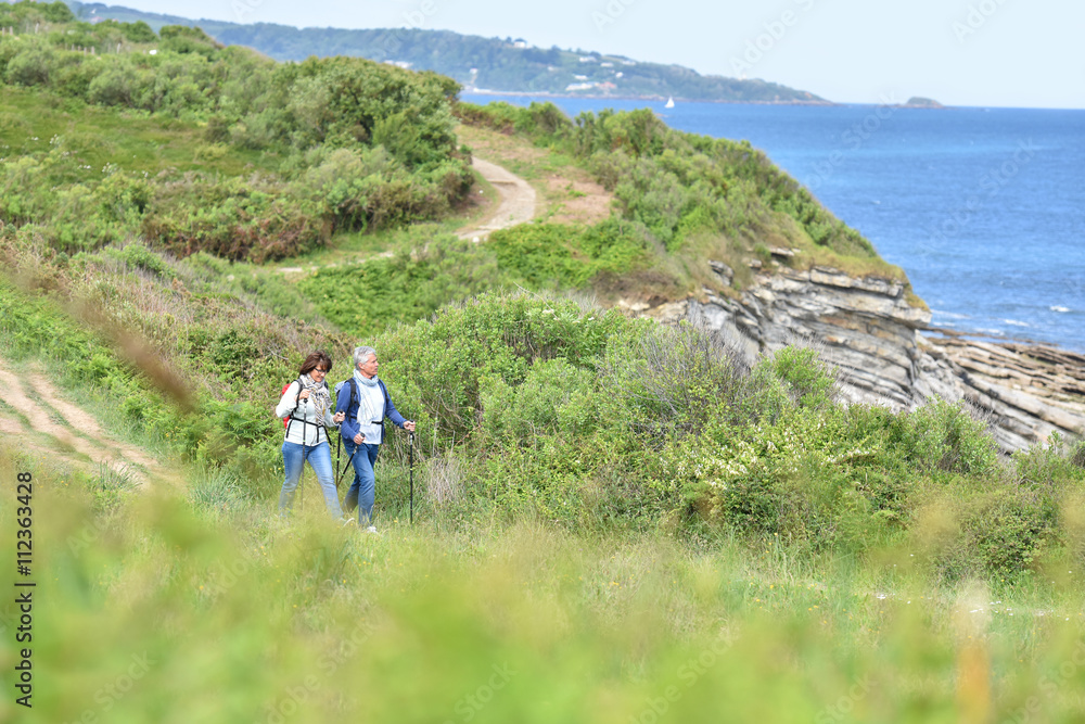 Obraz premium Senior couple walking on hiking track by the coast