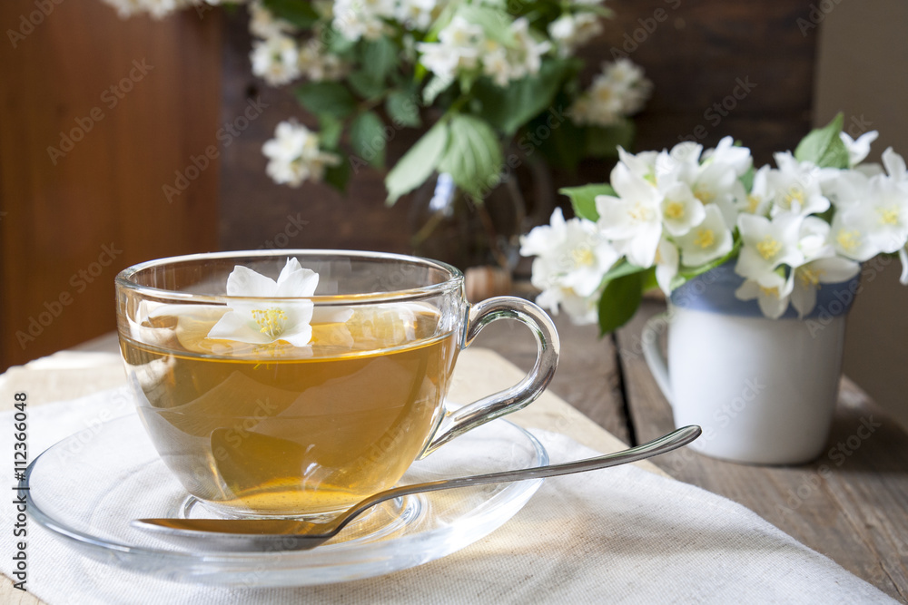 Transparent glass cup of tea with jasmine and blooming jasmine branch in blue ceramic cupon wooden board Transparent glass cup of tea with jasmine and blooming jasmine branch in blue ceramic cupon wooden board