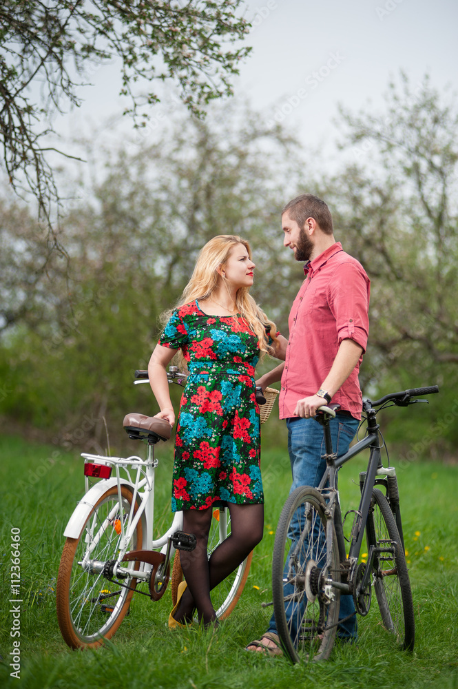 Loving young couple with bicycles against the background of trees and fresh greenery in spring garden. Couple together enjoying romantic holidays