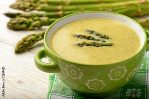 Green asparagus cream soup on wooden background.