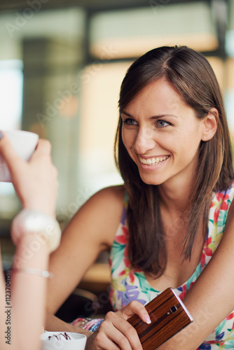 Two girls in a coffee shop, smiling, drinking coffee, smartphone in hand