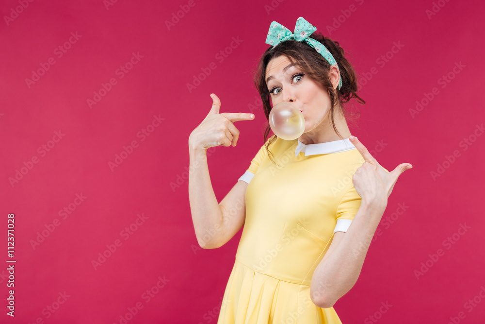 Playful charming young woman pointing on bubble gum balloon