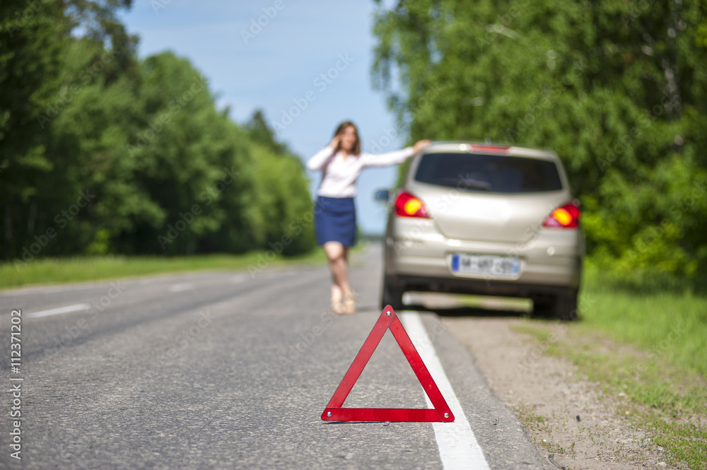 Triangle warning sign on the road and woman with her car after b