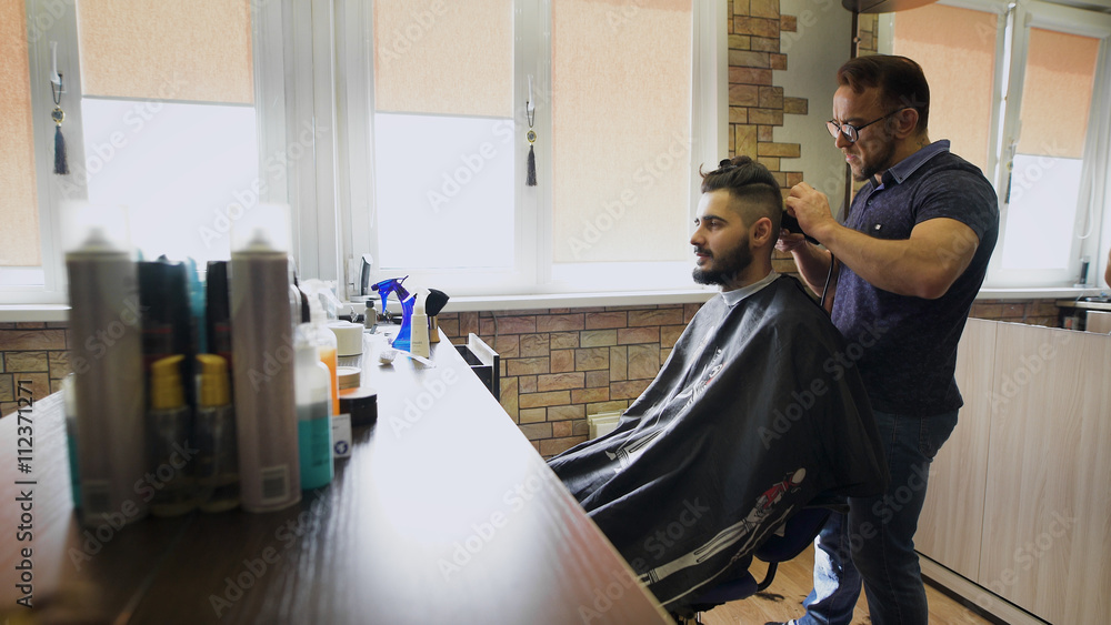 Getting groomed. Shot of a handsome bearded barber giving a haircut to his client using trimmer Getting groomed. Shot of a handsome bearded barber giving a haircut to his client using trimmer