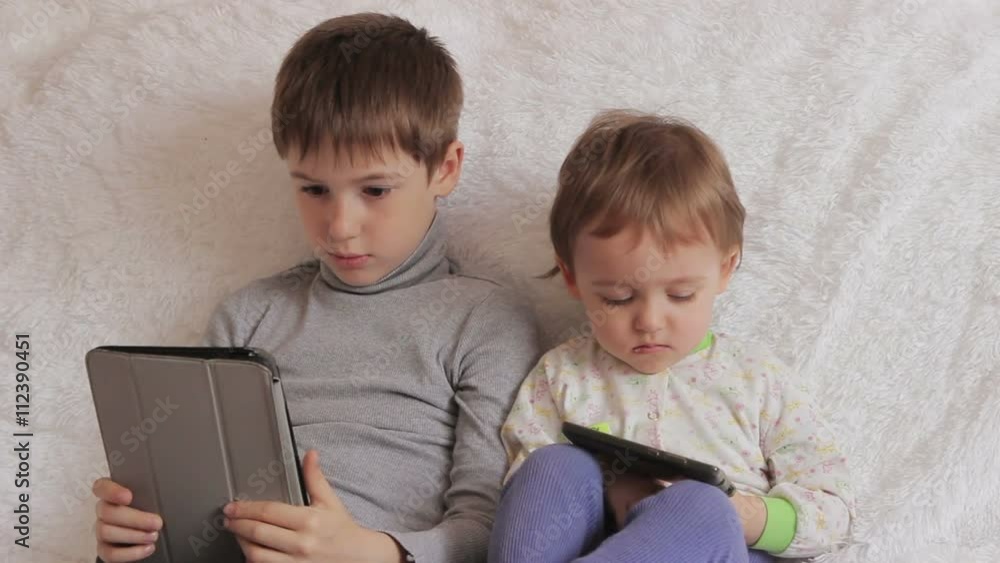 Children sitting on the couch playing on your tablet and phone to computer games Children sitting on the couch playing on your tablet and phone to computer games