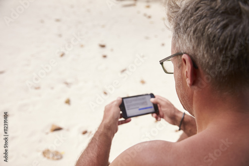 Man using a smartphone on a beach, over shoulder view