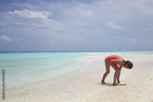 Young girl collecting sea shells on a white sand beach