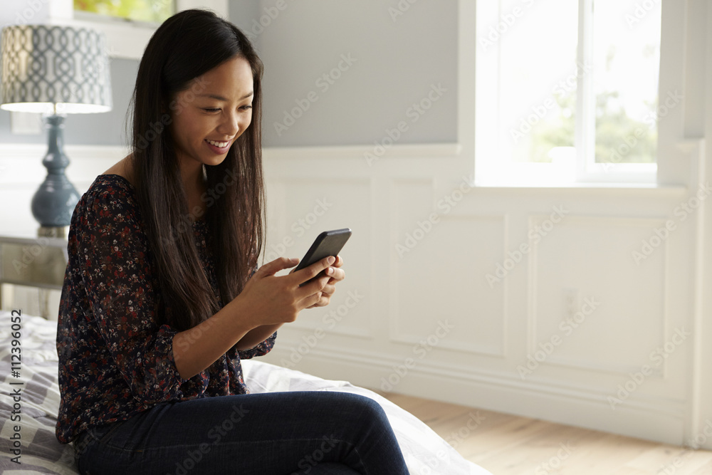 Woman Sitting On Bed In Bedroom Checking Mobile Phone Woman Sitting On Bed In Bedroom Checking Mobile Phone