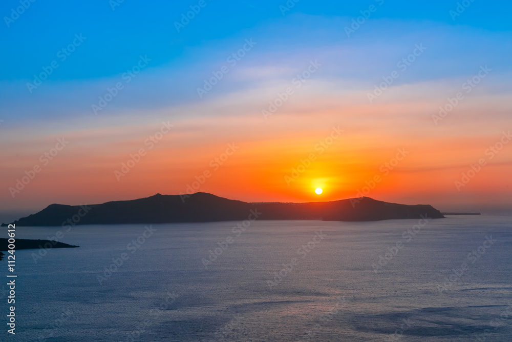Beautiful vibrant sunset over the sea and island Thirasia, Santorini, Greece