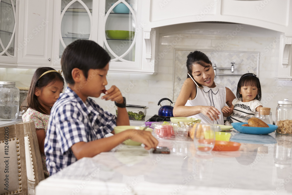 Busy Mother Organizing Children At Breakfast In Kitchen Busy Mother Organizing Children At Breakfast In Kitchen