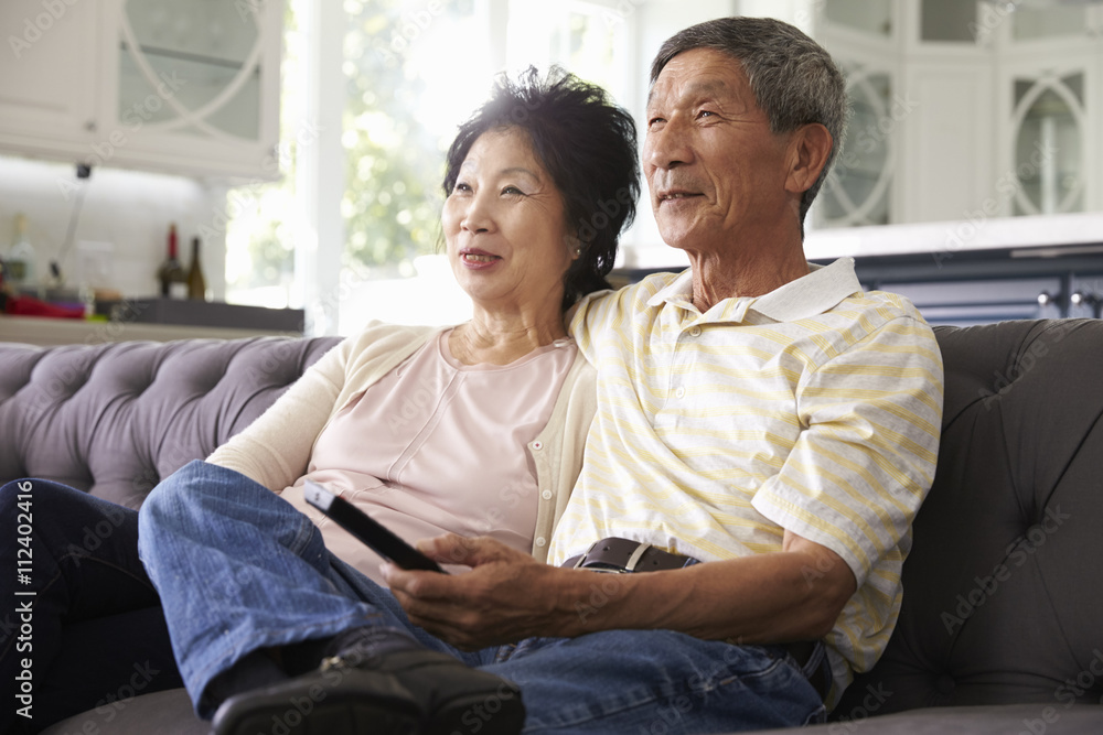 Senior Asian Couple At Home On Sofa Watching TV Together Senior Asian Couple At Home On Sofa Watching TV Together