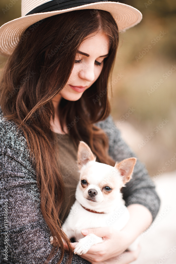 Smiling young girl wearing hat holding chihuahua outdoors. Woman with pet dog. Smiling young girl wearing hat holding chihuahua outdoors. Woman with pet dog.