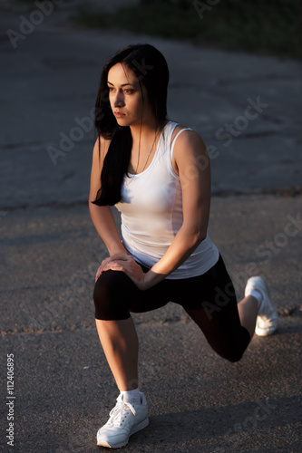 Sporty woman stretching on asphalt at sunset