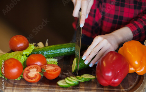 cooking and home concept - close up of female hand cutting vegetable on cutting board with sharp knife