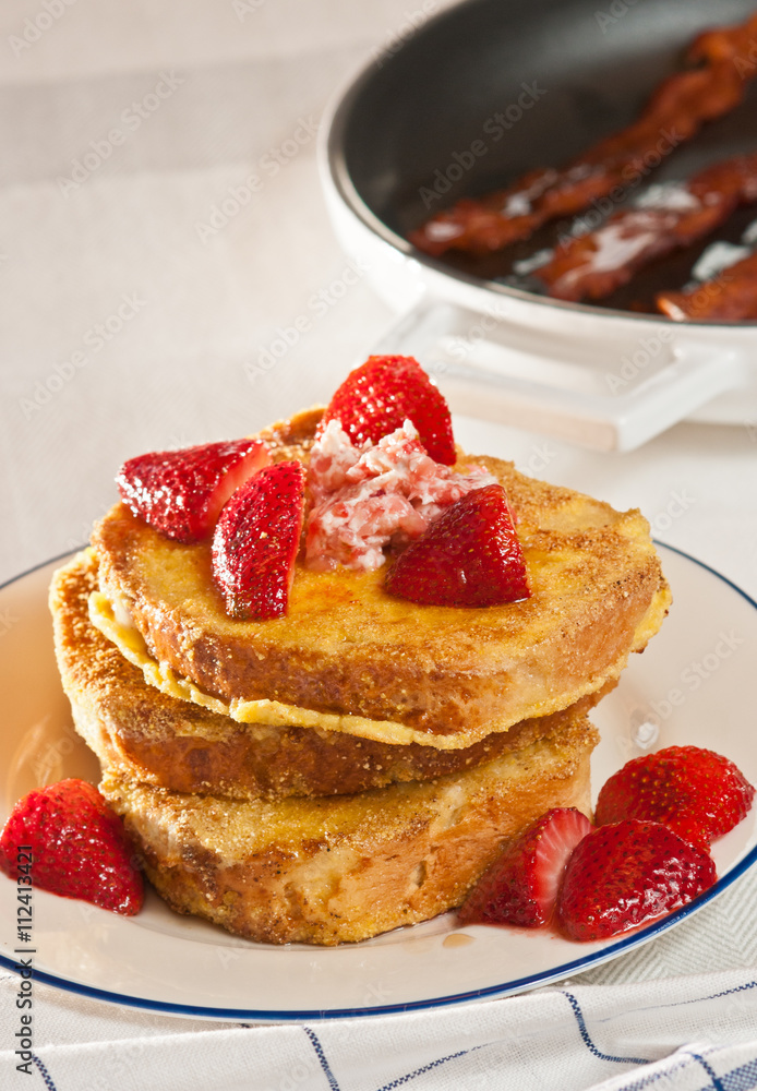 French toast with fresh strawberries and grilled bacon in background French toast with fresh strawberries and grilled bacon in background