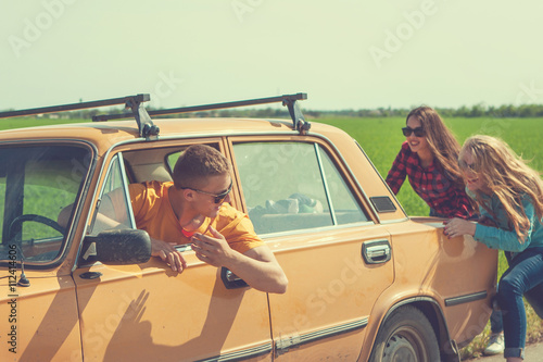 Young hipster friends on road trip on a summers day. Engine break down.Two girls pushing a vintage car while man is emboldening their.Travel, adventure, unforeseenteamwork, funny concept