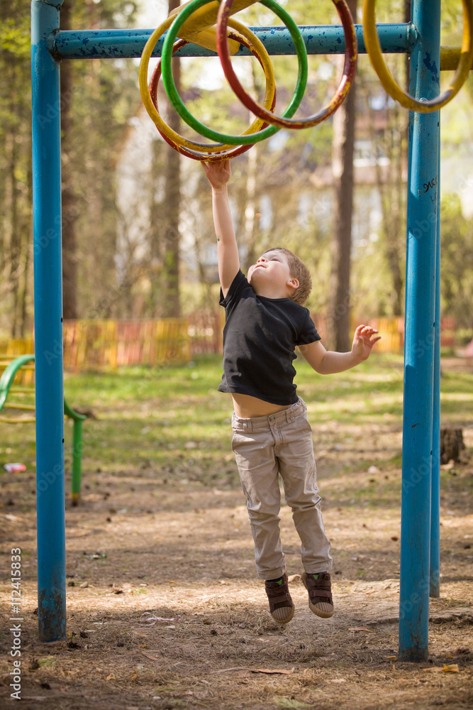 Obraz premium Portrait of cute kid boy jumping on the climbing frame. Young boy climbing on playground during summer. Child enjoys climbing in a children's playground outdoors.