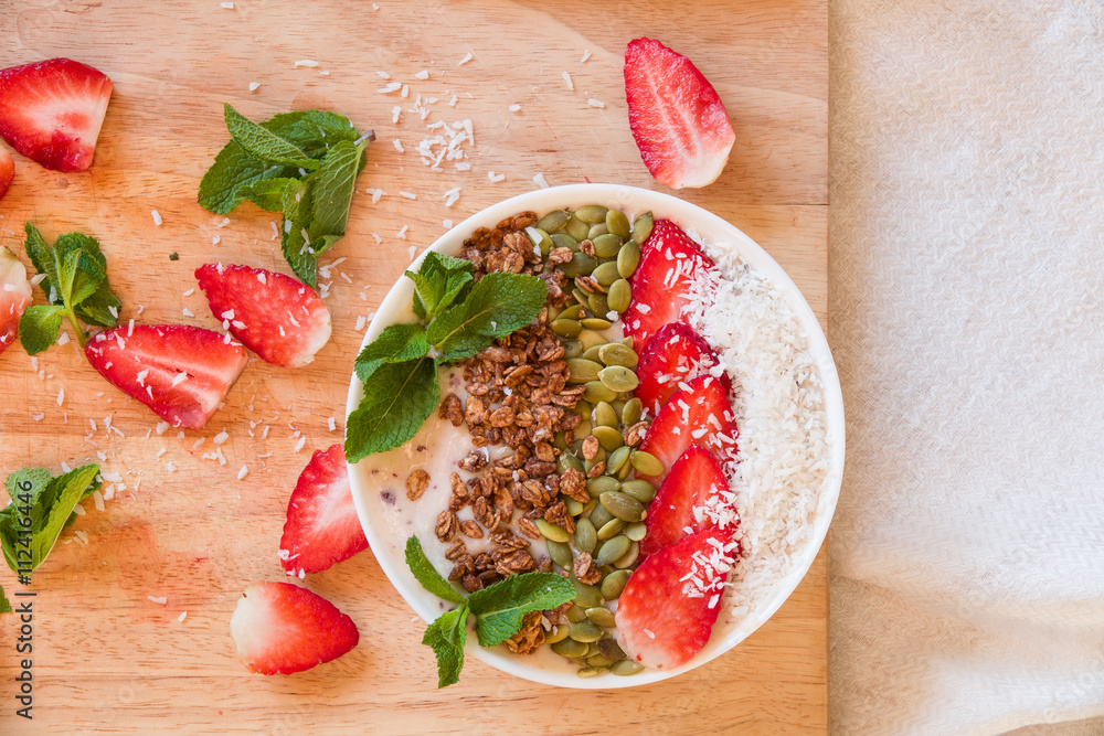 Breakfast berry smoothie bowl topped with strawberry, pumpkin seeds, coconut, muesli and fresh mint. Strawberry banana smoothie bowl. healthy breakfast or snack, wooden tableware. Breakfast berry smoothie bowl topped with strawberry, pumpkin seeds, coconut, muesli and fresh mint. Strawberry banana smoothie bowl. healthy breakfast or snack, wooden tableware.