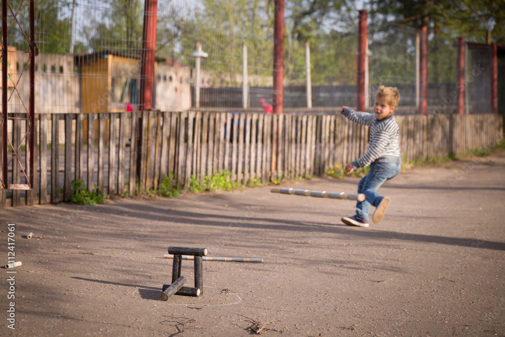 kid boy playing skittles in the street. Russian game skittles. Wooden skittles. Outdoor activites with children. Child playing in the sun.