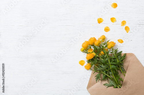 Top view on beautiful yellow garden flowers in the craft envelope on the white wooden background. Bouquet of flowers. Card. Greetings. Holidays and spring concept