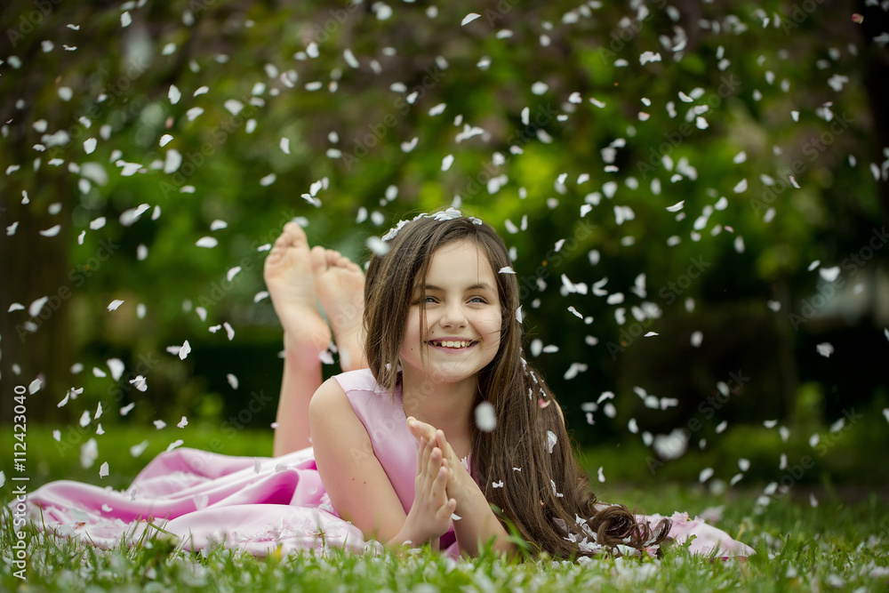 Little girl on green grass with petals