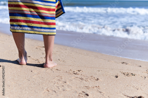 Person wearing towel walking along sand beach, closeup ol legs. sunny background outdoors © aquar
