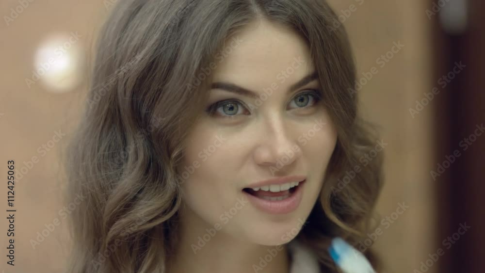 Beautiful woman in the bathrobe standing in the bathroom and brushes her teeth in the morning Beautiful woman in the bathrobe standing in the bathroom and brushes her teeth in the morning