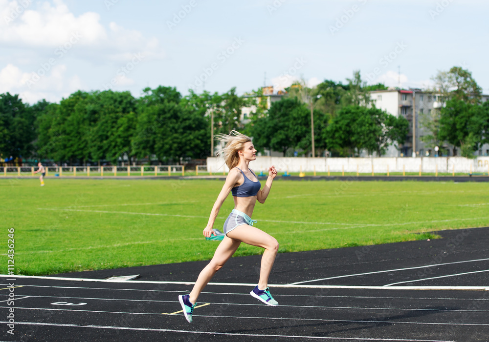 The sportswoman runs on a path at stadium.