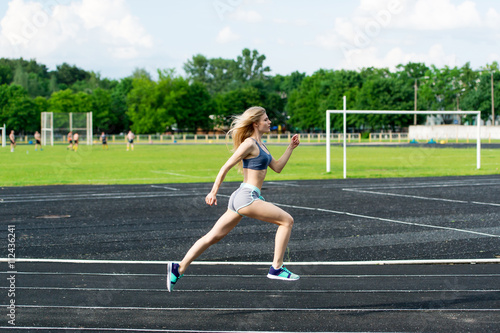 The sportswoman runs on a path at stadium.