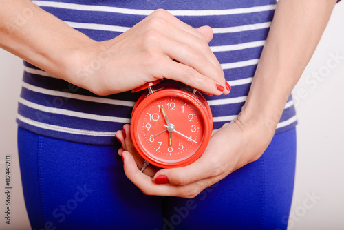 Female holding red alarm clock feeling stomach pain or hunger. 