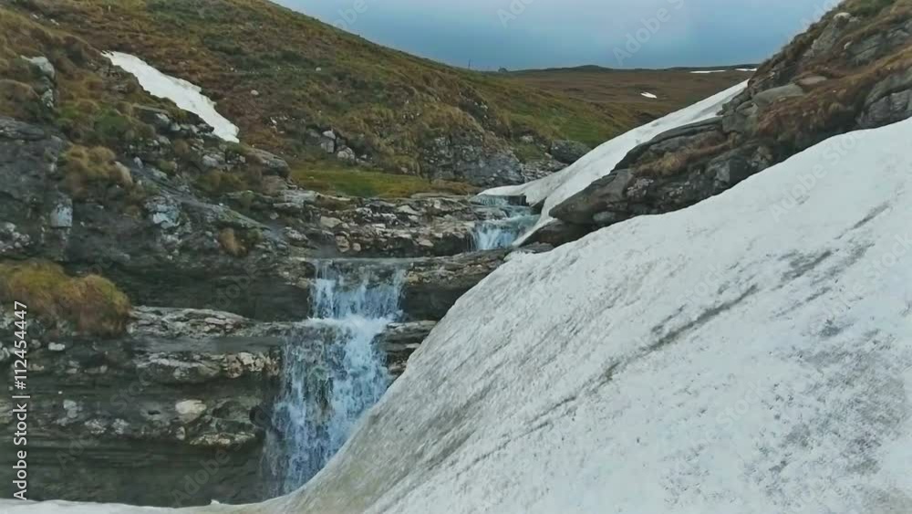 Slow motion shot of a mountain waterfall in spring with snow melting
