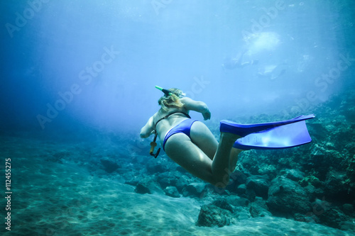 A woman floats in the ocean with fins in the background of pitfalls. Rear view under water