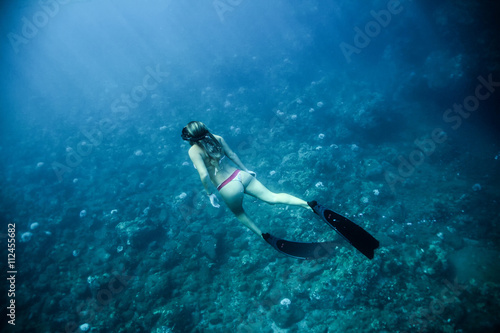 Woman in bikini and fins swims along the bottom of the ocean