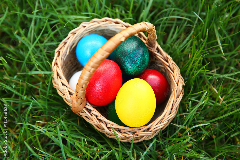 Basket with coloured Easter eggs on green grass Basket with coloured Easter eggs on green grass