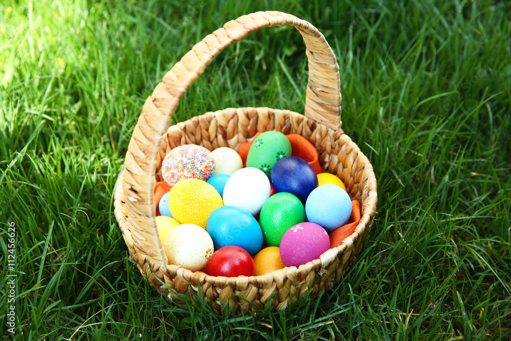 Basket with coloured Easter eggs on green grass