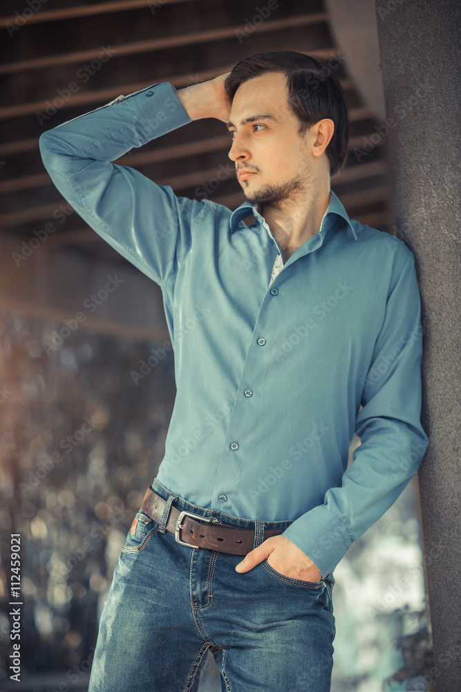 Young stylish man model in jeans and shirt posing in modern park architecture place. Fashion shot. Young stylish man model in jeans and shirt posing in modern park architecture place. Fashion shot.