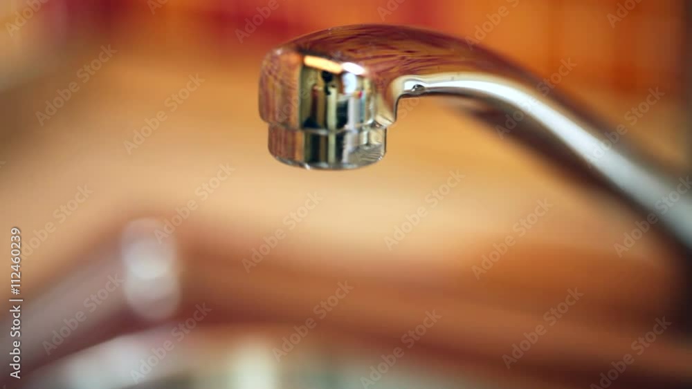 Closeup of water dripping from a kitchen tap - water wasting concept Closeup of water dripping from a kitchen tap - water wasting concept