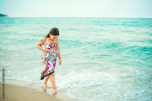 Child walking along the seacoast. Girl in a colorful dress walking on the beach
